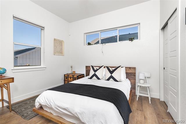 Bright bedroom with a wood bed frame, black-and-white bedding, high windows, and hardwood floors.
