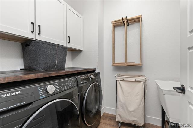 Laundry room with black front-loading washer and dryer, white cabinets, and a rolling hamper.