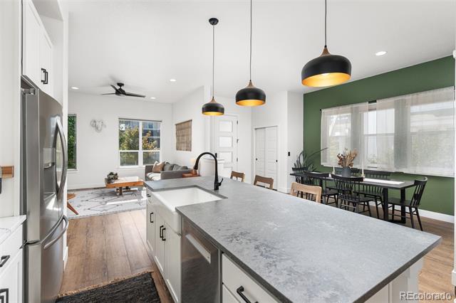 Open-plan kitchen with a large gray island, black pendant lights, and a green dining-area wall.