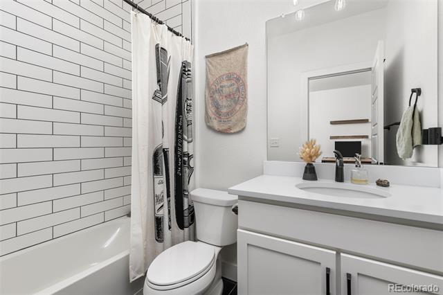Bathroom with white subway-tile tub surround, shower curtain, toilet, and wide vanity.