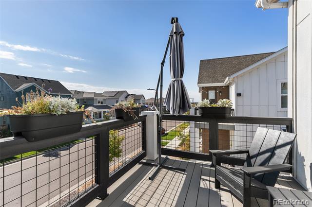 Home balcony with black mesh railings, lounge chairs, a closed umbrella, and flower planters.