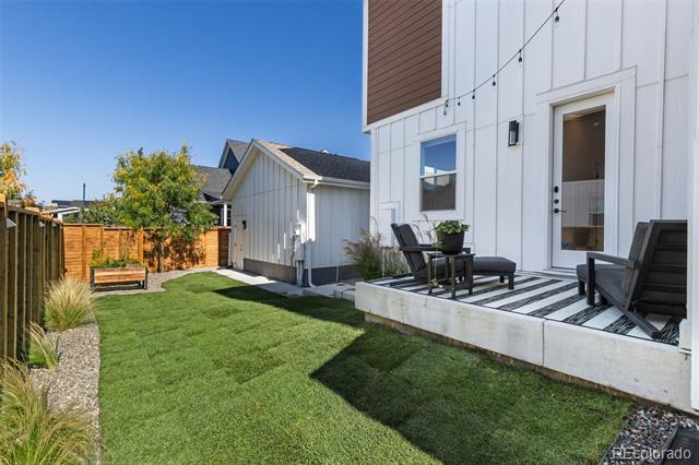 Backyard lawn and raised patio with black seating beside a white-sided home.