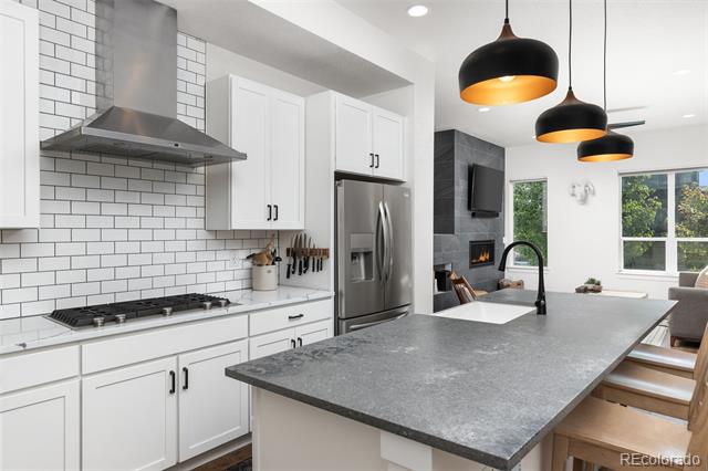 Modern kitchen with a large gray stone island, white cabinetry, subway tile, and three black pendant lights.
