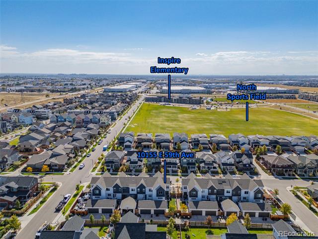 Aerial view of 10155 E 59th Avenue, with nearby homes, a sports field, and Inspire Elementary School.