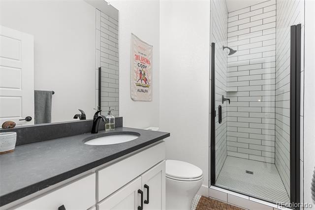 Modern bathroom with a glass-enclosed subway-tile shower and white vanity with dark countertop.