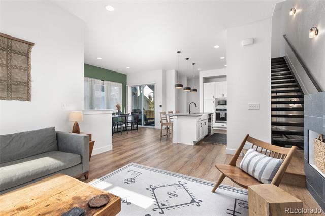 Open-plan living room and kitchen with light wood floors, green accent wall, and dark staircase.