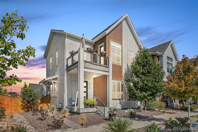 Modern two-story home with a balcony, wood-tone siding, and landscaped front patio at dusk.