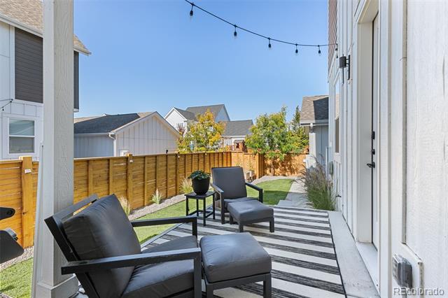 Furnished patio with black lounge chairs, a striped rug, and string lights beside the home.