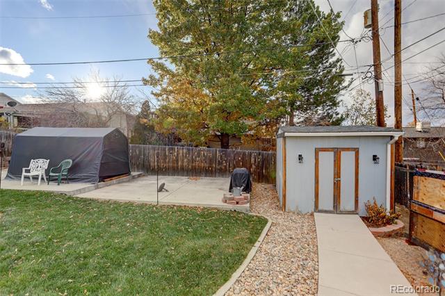 Backyard with a grassy lawn, gravel path, small shed, and covered outdoor structure.