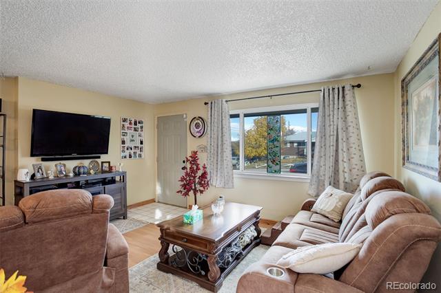 Living room with tan sofas, a carved wooden coffee table, and a large curtained window.