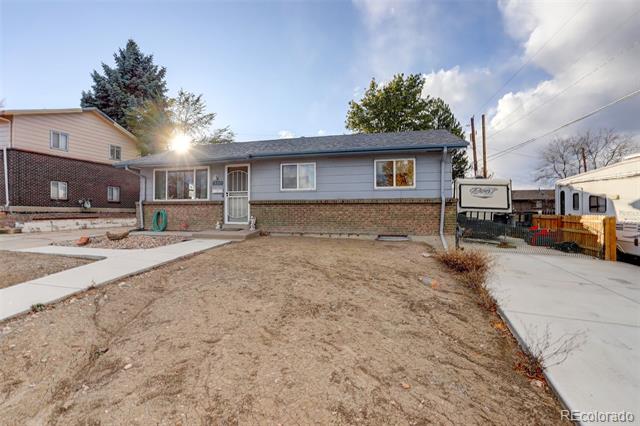 Gray single-story house with a brick foundation, bare dirt yard, and concrete driveway.