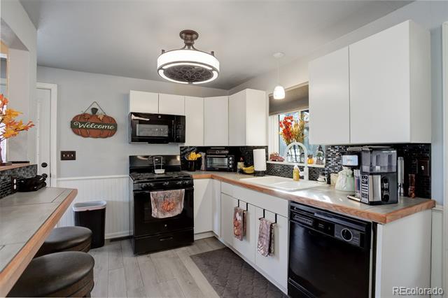 Kitchen with white cabinets, black appliances, gray tile backsplash, and a breakfast bar with dark stools.