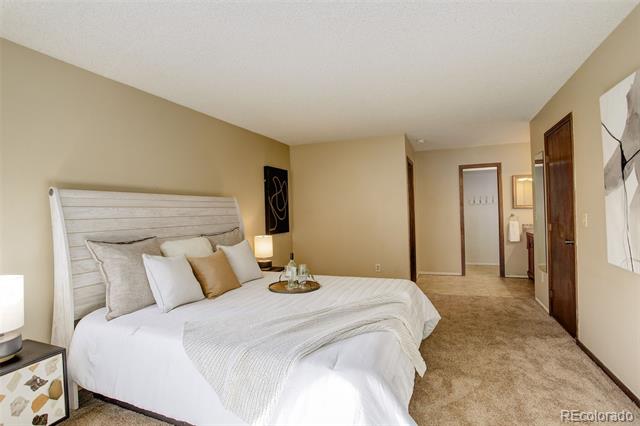 Furnished bedroom with a white bed, light upholstered headboard, and beige carpet.