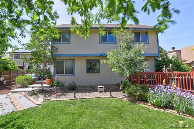 Two-story blue-gray house with a red-railed deck and flower beds behind a green lawn.