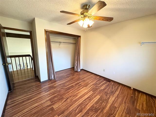 Empty bedroom with wood-look flooring, an open closet, and a ceiling fan.
