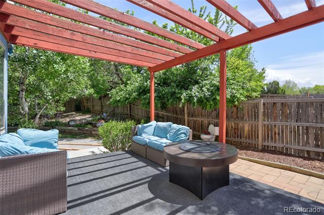 Backyard patio beneath a red pergola, with blue seating and a round fire-pit table.
