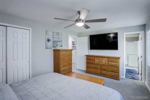 Bedroom with a gray bed, wooden dressers, wall-mounted TV, and ceiling fan.