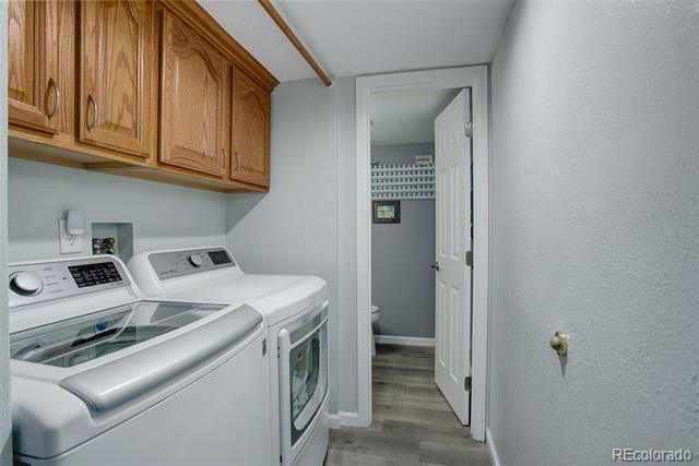 Laundry room with a front-loading washer and dryer beneath wood cabinets.