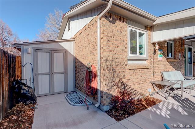 Brick house patio with outdoor chairs, a small storage shed, and fenced yard.