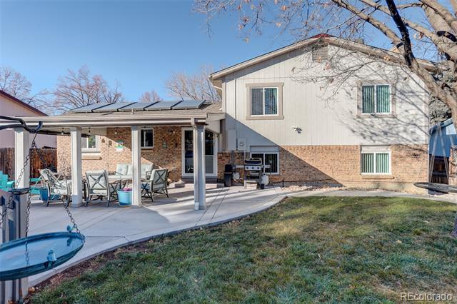 Home’s rear exterior with a covered, furnished patio, barbecue grill, and grassy backyard.