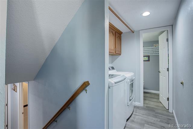 Laundry room with washer and dryer, wooden cabinets, and gray plank flooring beside a staircase.