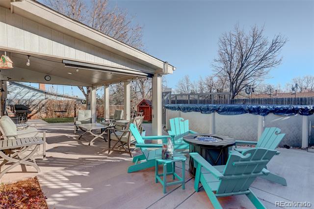 Covered patio with turquoise Adirondack chairs around a fire pit beside a swimming pool.