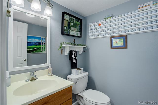 Bathroom with a wood-front vanity, white toilet, and shelves displaying golf balls.