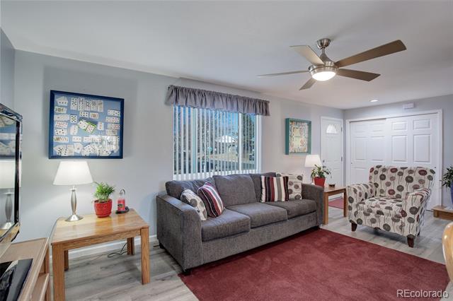 Living room with a gray sofa, patterned armchair, red rug, and ceiling fan.