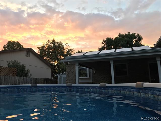 Backyard swimming pool beside a covered patio and solar-paneled roof at sunset.