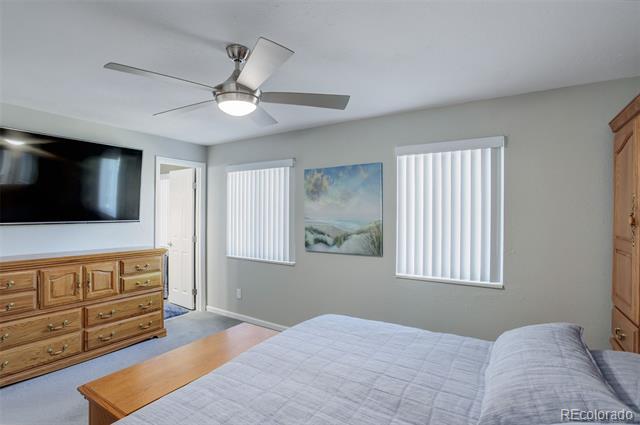 Bedroom with a ceiling fan, wall-mounted television, and wooden dresser beside the bed.