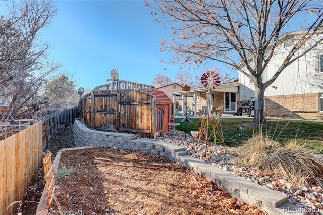 Backyard with a fenced raised wooden deck, decorative windmill, and stone-edged landscaping.