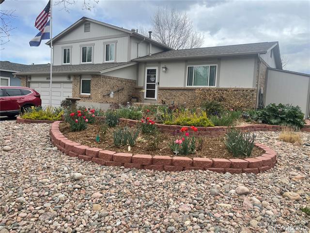 Two-story gray and stone house with an attached garage and a brick-edged flower garden.
