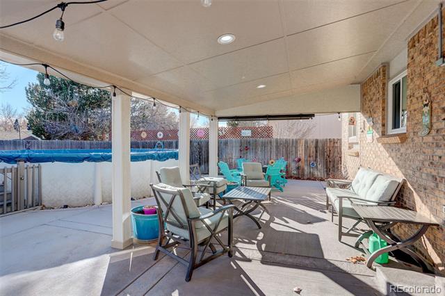 Covered patio with outdoor dining and lounge furniture beside a fenced swimming pool.