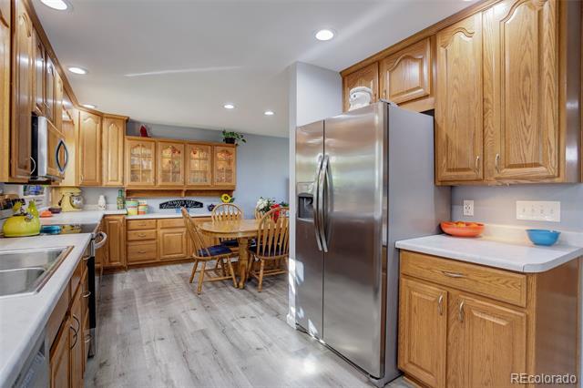 Kitchen with oak cabinets, stainless steel refrigerator, gray plank flooring, and a dining table.