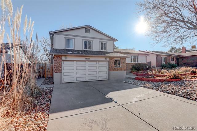 Two-story home with a white double garage, brick facade, and rock landscaping along a broad driveway.