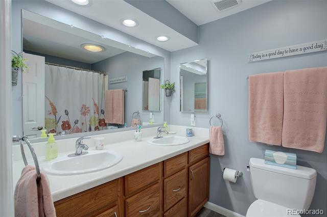Bathroom with a double-sink vanity, wood cabinets, floral shower curtain, and pink towels.