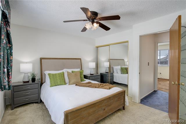 Bedroom with a wooden bed, green accent pillows, mirrored closet doors, and a ceiling fan.
