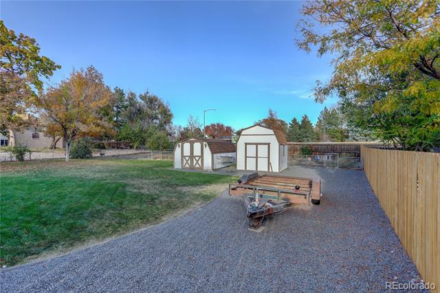 Backyard with two storage sheds, a gravel parking area, lawn, and utility trailer.