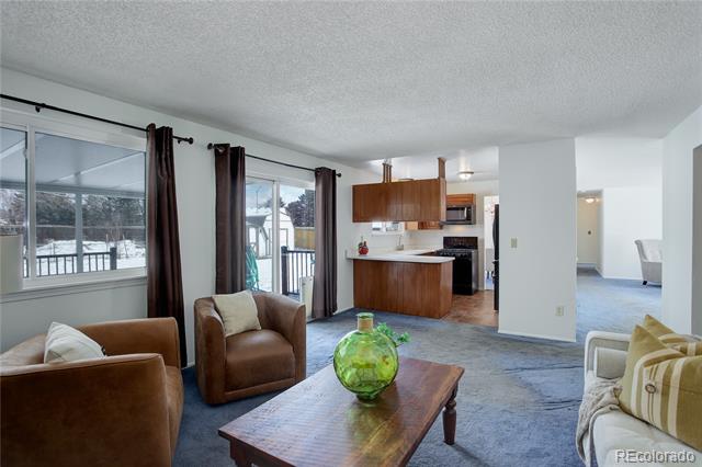 Living room with brown armchairs and a wood coffee table, opening to a kitchen beside snowy windows.