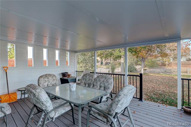 Covered porch with a glass-top dining table and cushioned chairs overlooking a fenced, leaf-strewn yard.