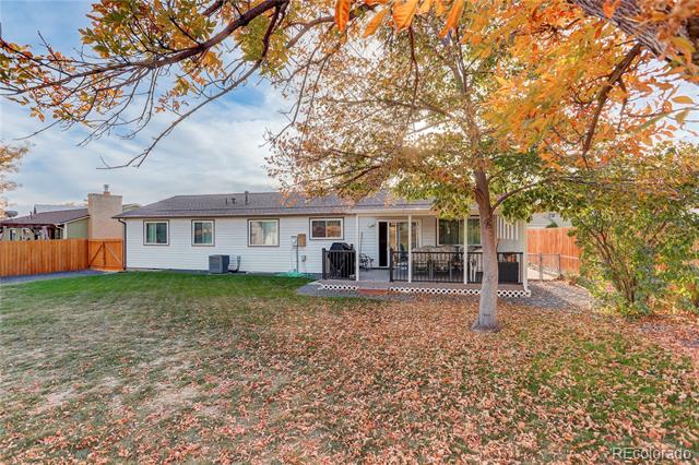 Single-story home with a raised deck and fenced backyard beneath a large orange-leaved tree.