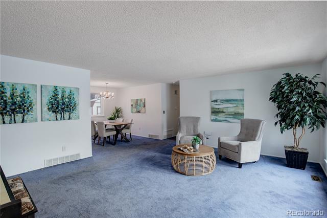 Living room with blue carpet, wicker coffee table, gray armchairs, and dining area beyond.