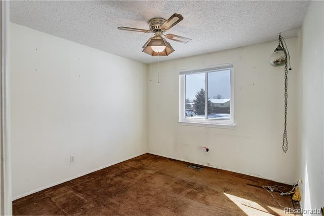Empty bedroom with worn brown carpet, ceiling fan, and a window overlooking snowy ground.