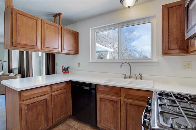 Kitchen with reddish wood cabinets, white countertops, a sink beneath a window, and a stainless steel gas range.