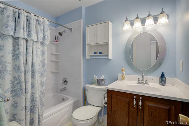 Bathroom with a floral shower curtain, white tub and toilet, and dark wood vanity beneath an oval mirror.