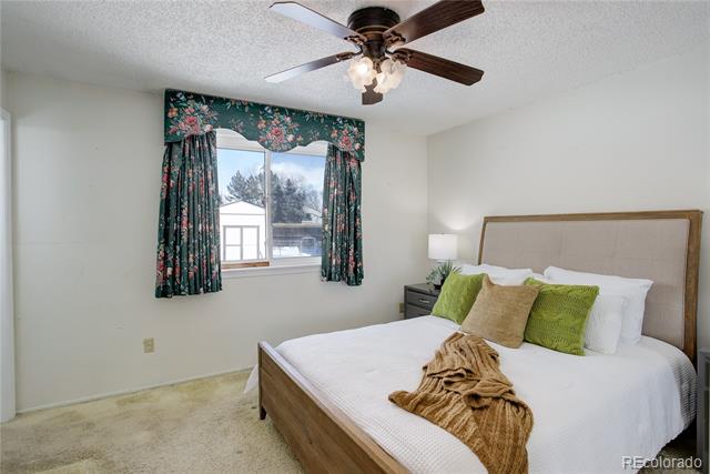 Bedroom with white bedding, green pillows, floral curtains, and a ceiling fan.