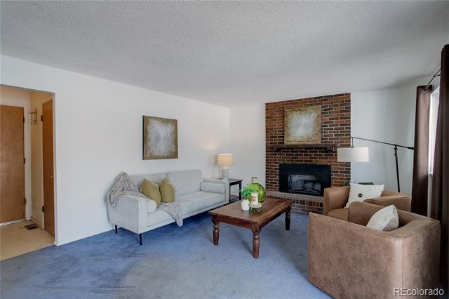 Living room with blue carpet, a brick fireplace, a light sofa, and two brown armchairs.