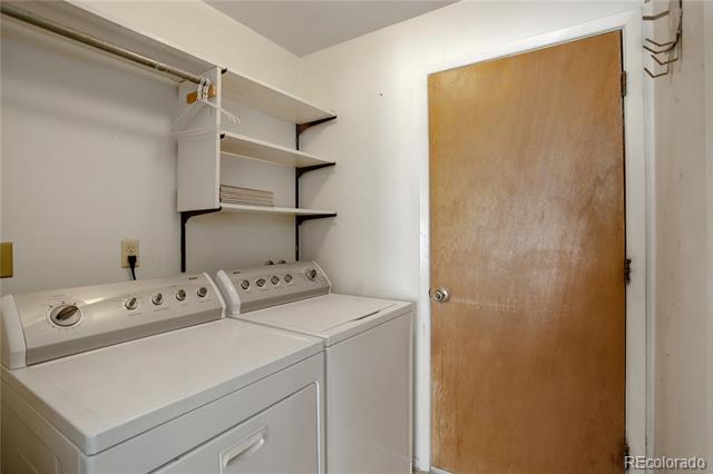 Laundry room with a white washer and dryer beneath open storage shelves.