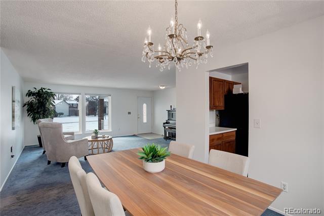 Dining area with a long wooden table and chandelier overlooking the living room and snowy yard.