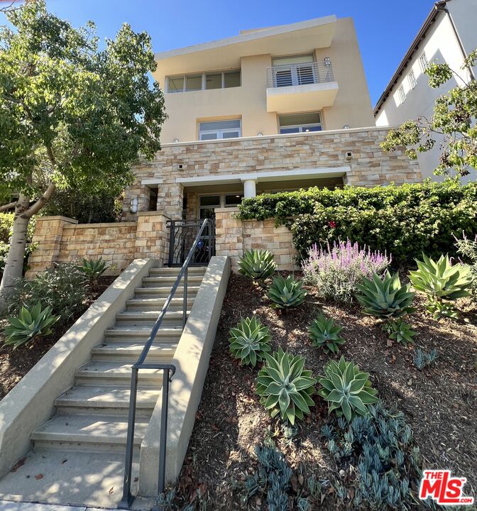 Modern stone-fronted home above landscaped steps with succulents and flowering plants.